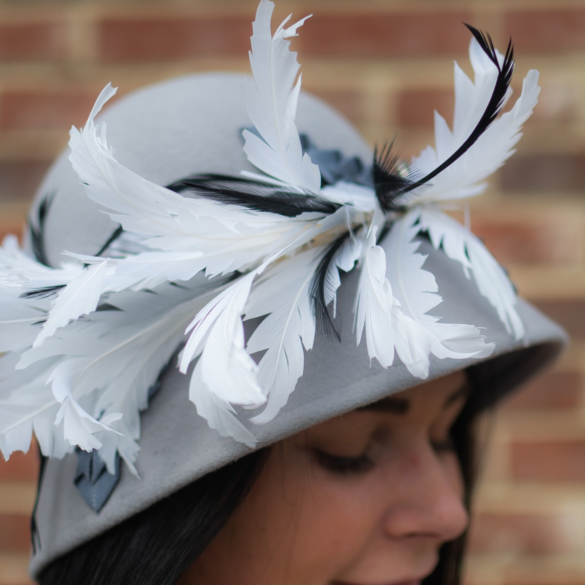 Lady wearing a grey cloche hat with white and black feathers