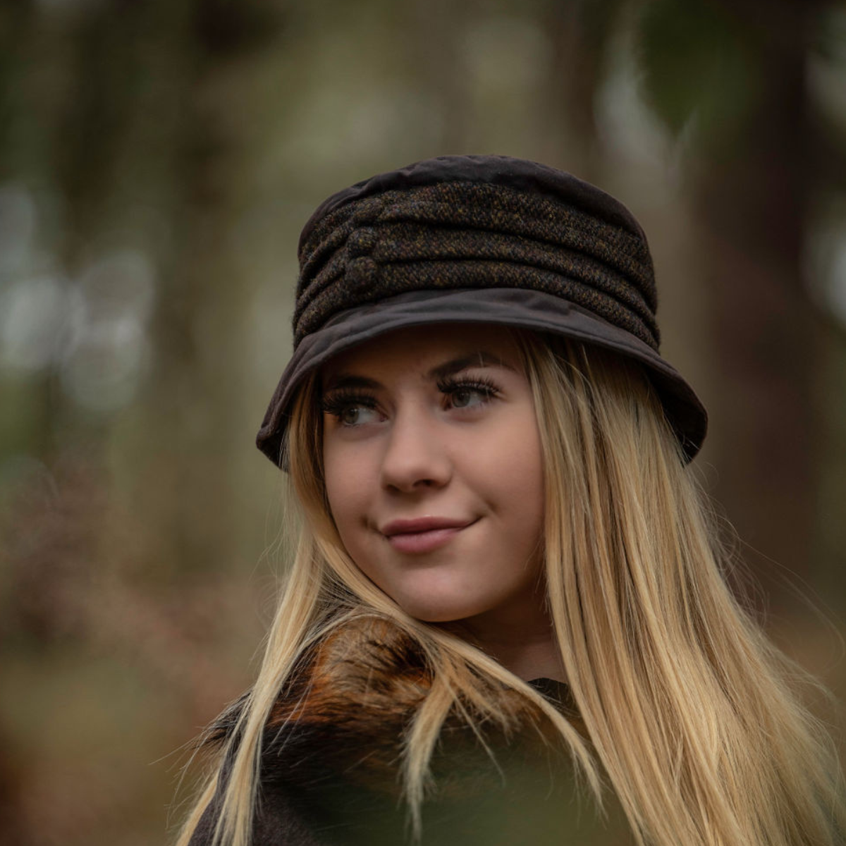 A lady in the woods with a waxed rain hat on her head