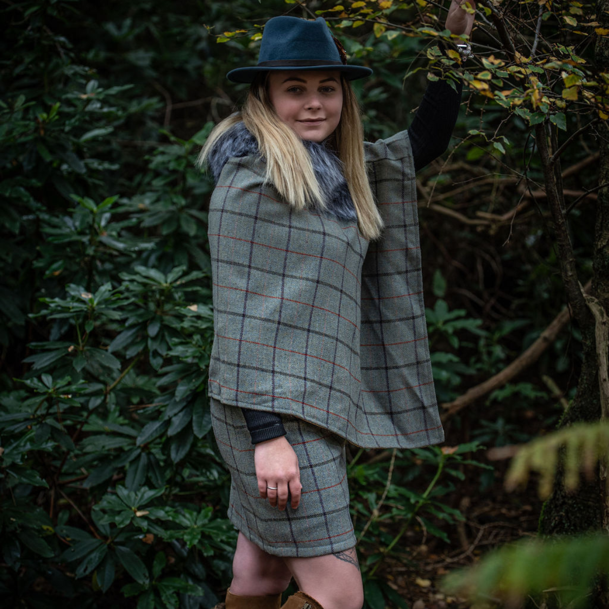 Lady standing by a tree wearing a tweed skirt and poncho